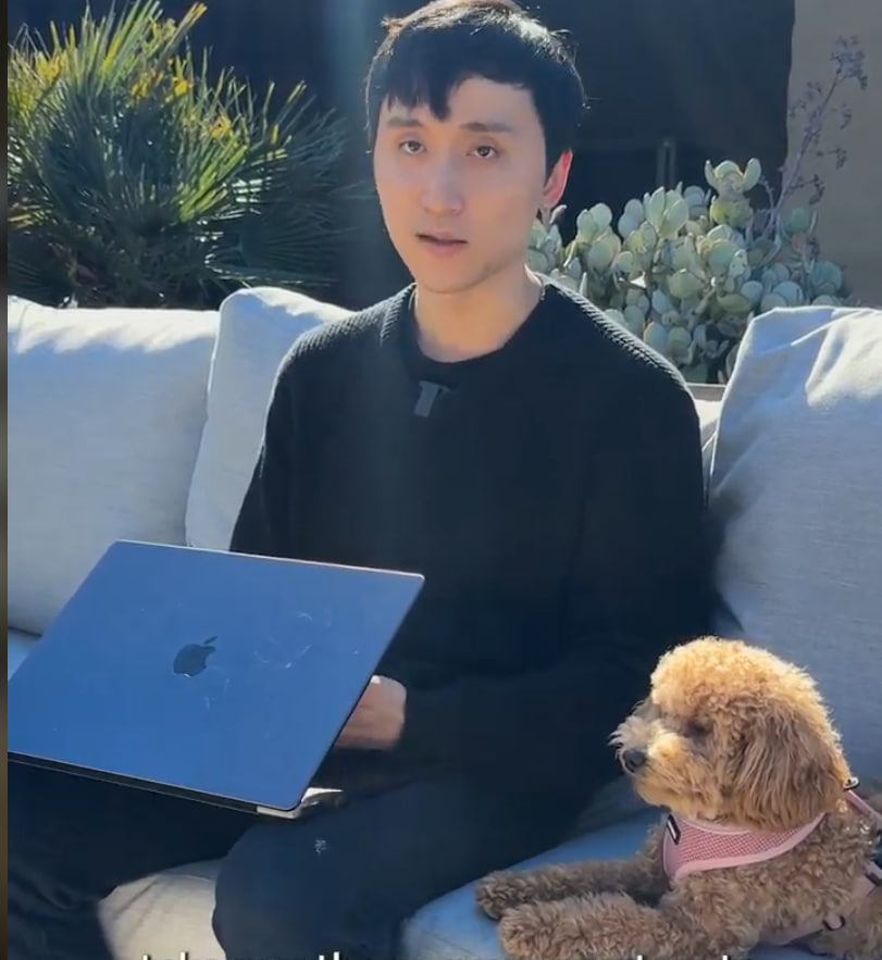 Coco, a toy poodle in a pink harness, sitting on a couch next to the Robinhood crypto engineer working on a laptop.